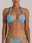 Close-up front view of a woman wearing a shimmering light blue halter bikini with ruched triangle cups and knot-tie bikini bottom.