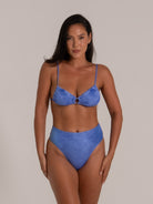 Front view of a model in a textured blue bikini set featuring a ring detail at the bust and high-waist bottoms.