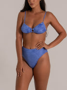 Model showcasing a blue high-waisted bikini set with textured fabric and center ring design, side pose