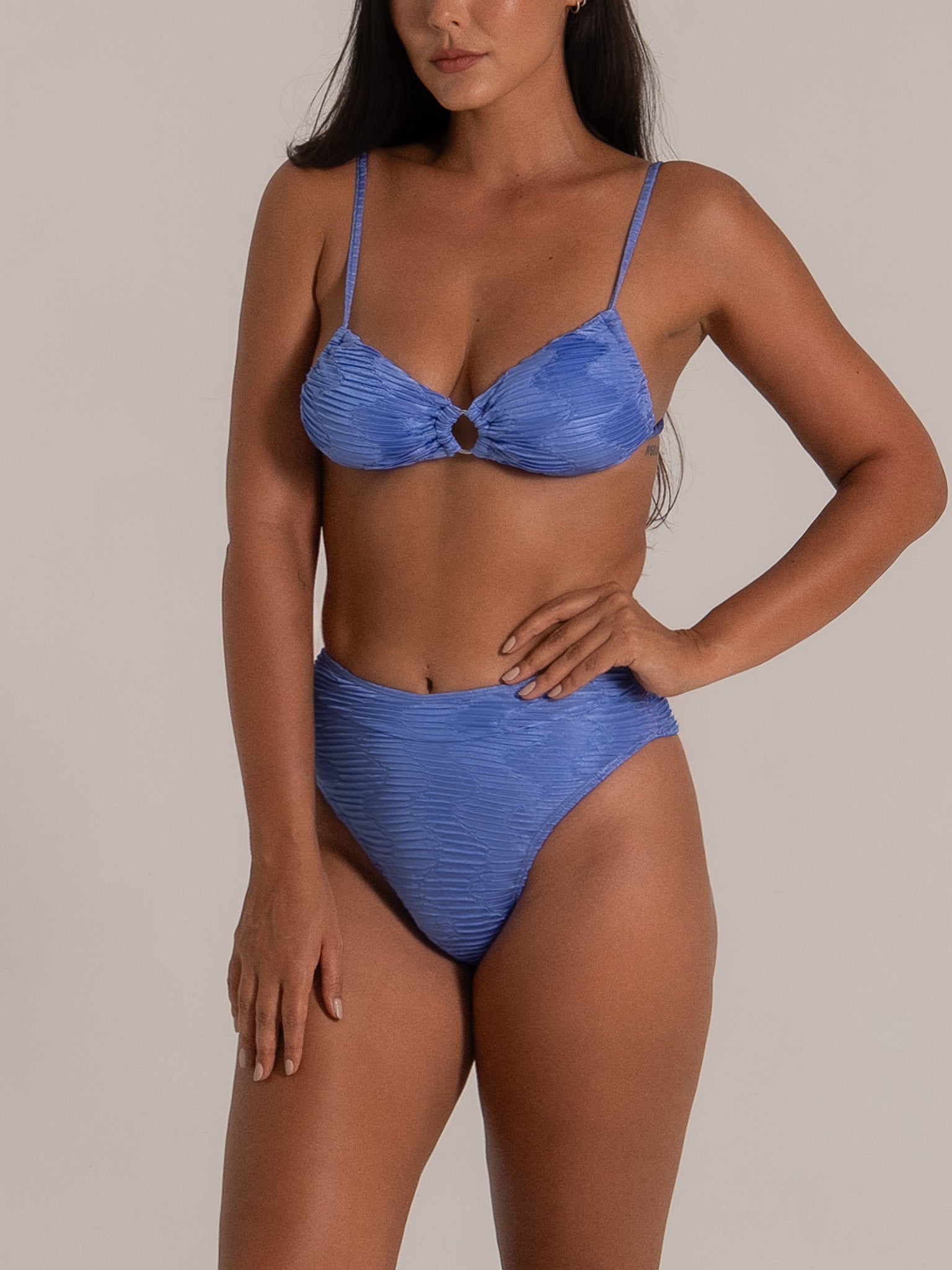 Model showcasing a blue high-waisted bikini set with textured fabric and center ring design, side pose