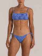 Woman wearing a blue textured bikini with spaghetti straps and tie-side bottoms, front view