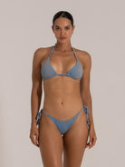 Front view of a woman in a blue textured triangle bikini, featuring halter neck and tie-side bottoms.