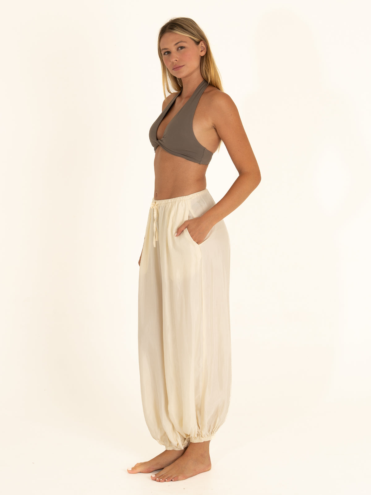 Woman styling a charcoal gray twist bikini top with loose white linen pants for a quiet luxury resort look, side view.