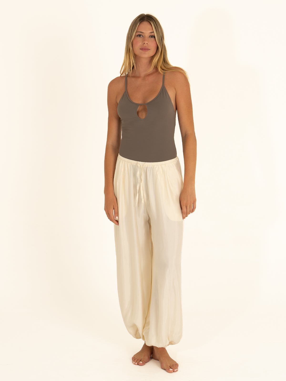 Effortless resort styling showing a charcoal gray keyhole one-piece swimsuit worn as a bodysuit with white linen pants.