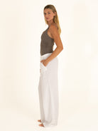 Side view of a woman styling the charcoal gray one-piece swimsuit as a bodysuit with flowy white linen trousers.