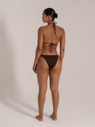 Back view of model wearing chocolate brown halter neck triangle bikini set with tie sides