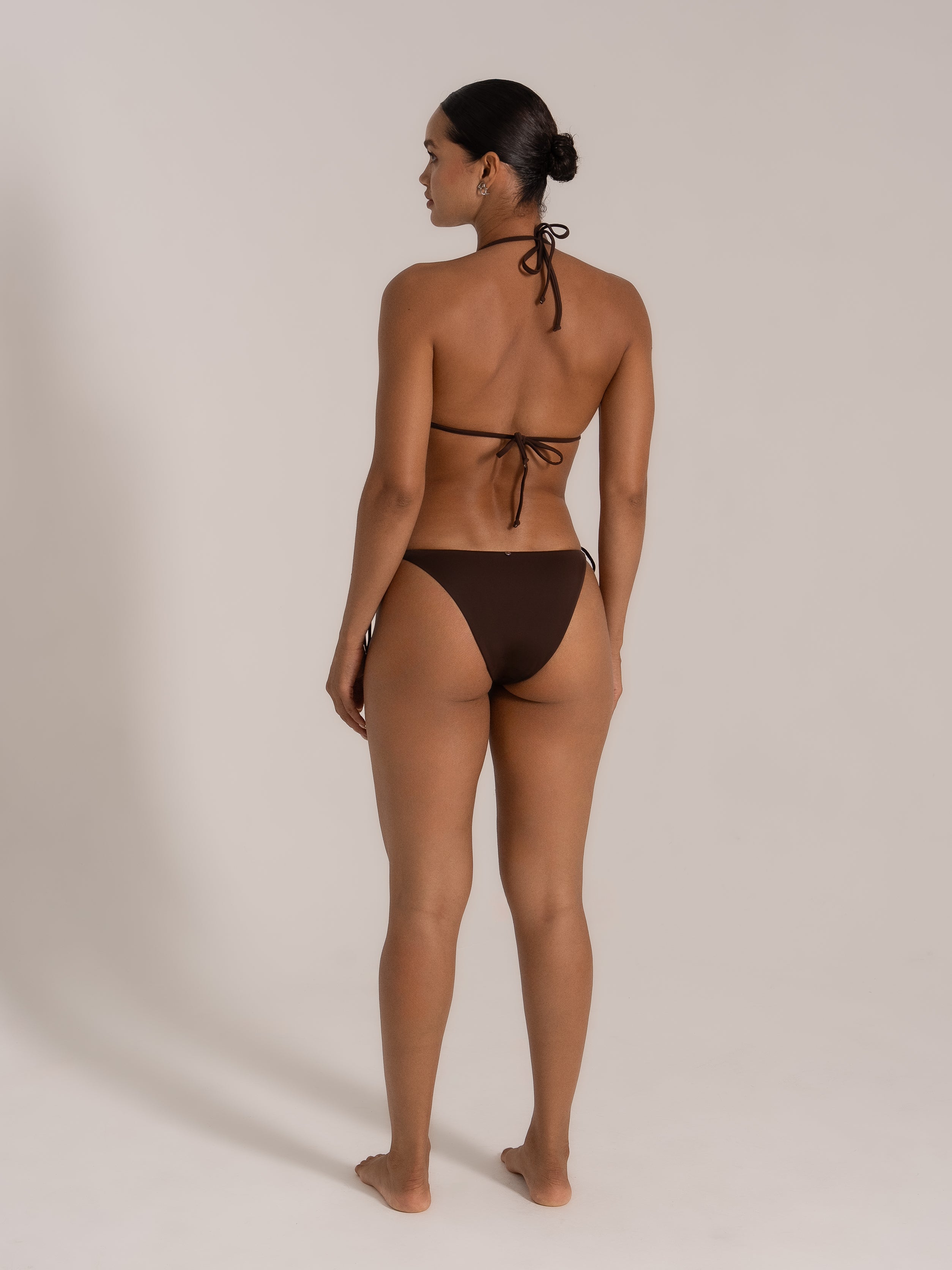 Back view of model wearing chocolate brown halter neck triangle bikini set with tie sides