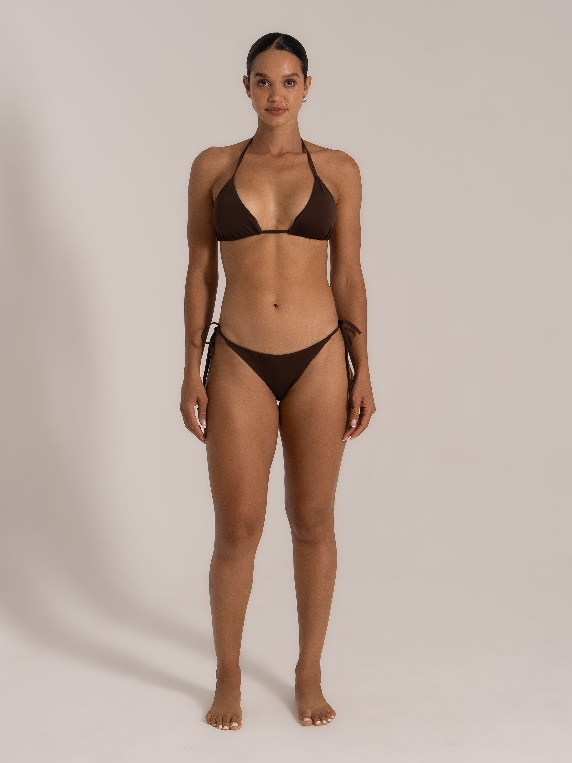 Front view of model in chocolate brown triangle bikini top with halter tie and low-rise tie side bottoms