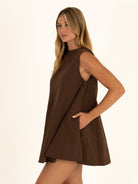 Side profile of a woman wearing the high neck side of the chocolate brown cotton dress, utilizing the adaptable reversible side pockets.