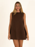 Front view of the chocolate brown reversible dress worn reversed on the high neck side, offering a clean, minimalist resort aesthetic.