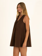 Side angle view of the chocolate brown cotton mini dress, highlighting the flowy A-line trapeze silhouette and ruched V-neck design.