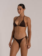 Model in brown bikini set with triangle top and side-tie bottom, angled pose.