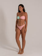 Model wearing a color-block pink and mint green bandeau bikini with gold ring detail