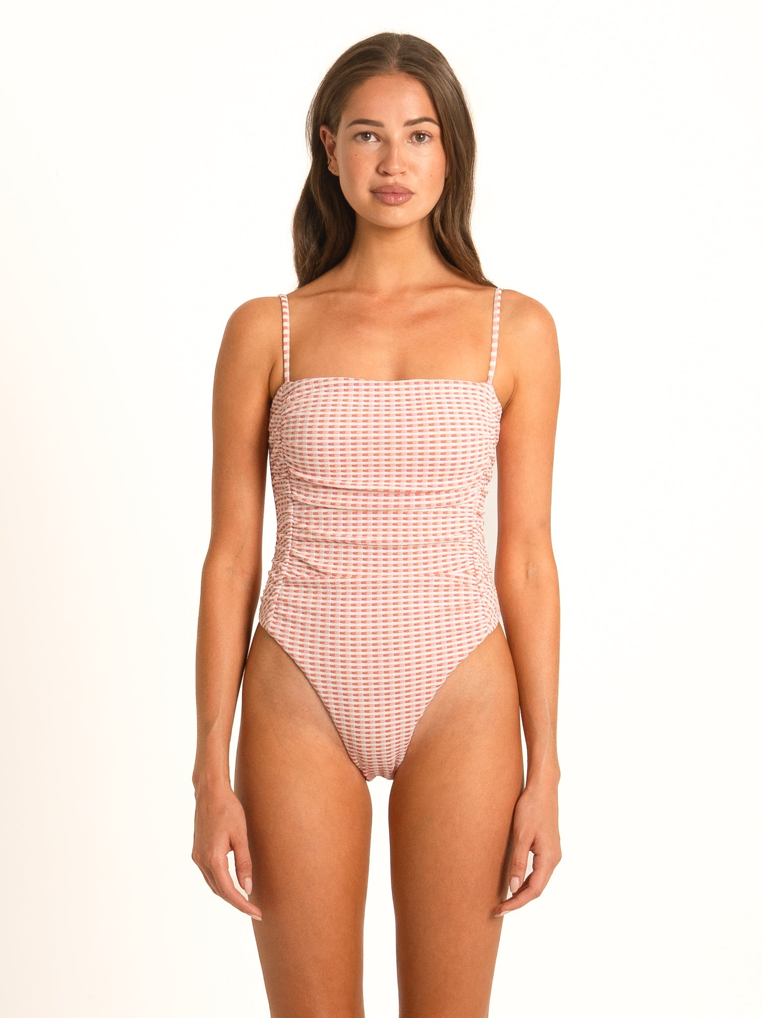 Front view of the Coral Gingham Shirred One-Piece on a model, showcasing the retro square neckline and tummy smoothing full body ruching in peachy pink and white.