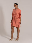 Side angle of coral orange short dress featuring adjustable waist tie