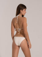 Back angled view of a woman in a white string bikini with side-tie bottoms and halter neck straps.