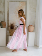 Elegant woman in a V-neck long dress featuring white and pink pleated details and a black sequin belt.