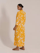 Back angled view of a model in a yellow floral shirt dress with long sleeves