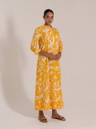 Side view of a woman in a yellow and white floral maxi dress with button-up collar