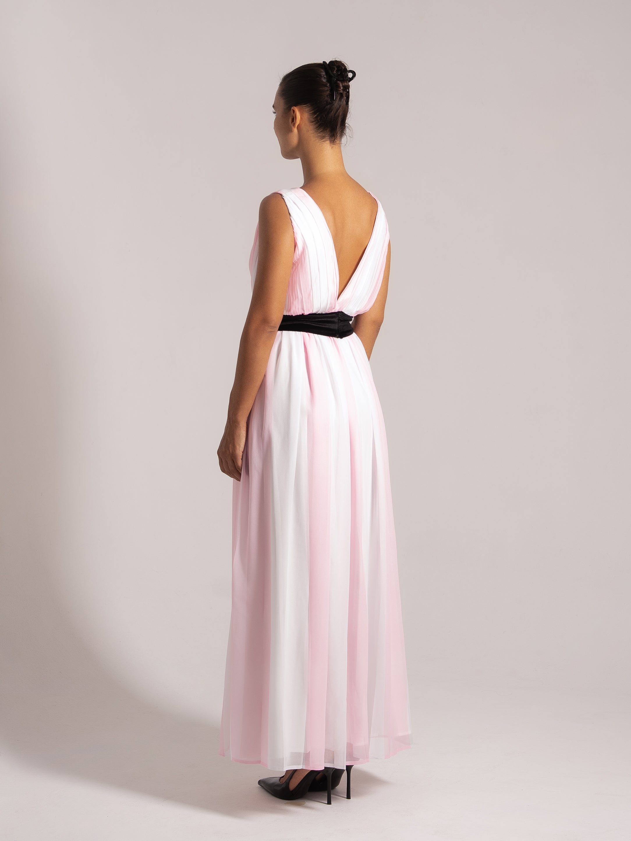 Back angle showing the deep V-back and flowing fabric of a pink and white pleated maxi dress.