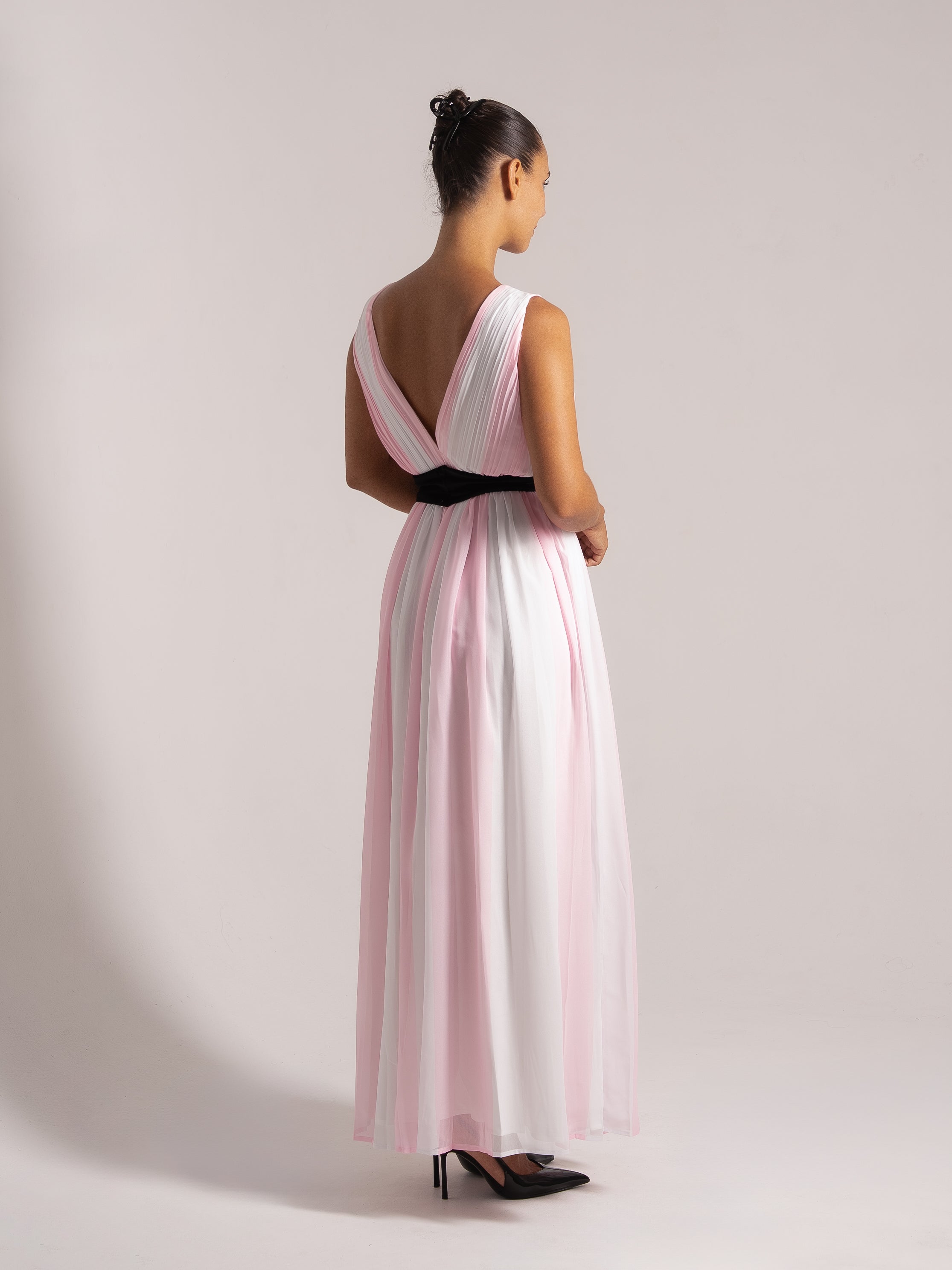 Back-side perspective of a flowing pink and white ombre maxi dress with structured pleats and a statement belt.