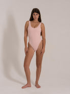 Front view of a woman wearing a pastel pink ribbed one-piece swimsuit with a scoop neckline and high-cut legs.