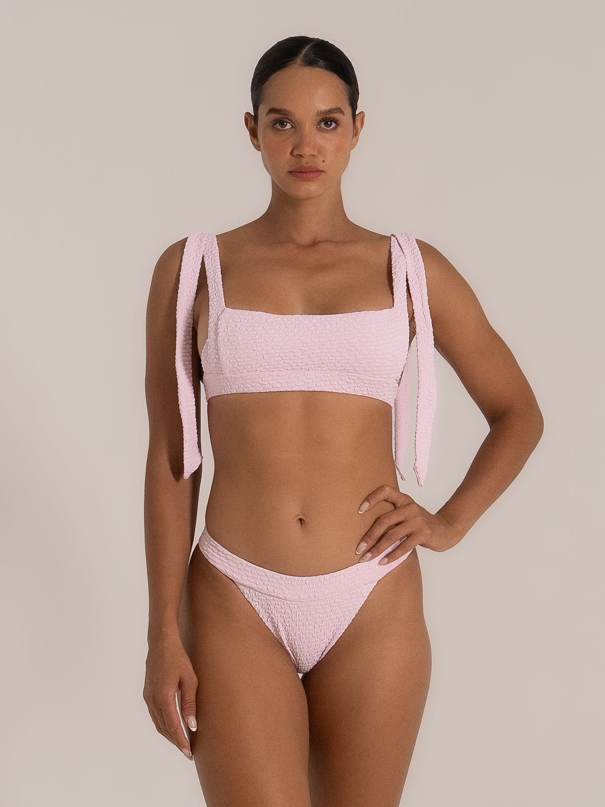 Model wearing pink tie strap bikini top with matching textured bottom, front full view