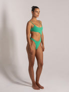 Model in green cut-out one-piece swimsuit with side ring detail, side profile displaying high-cut legs.