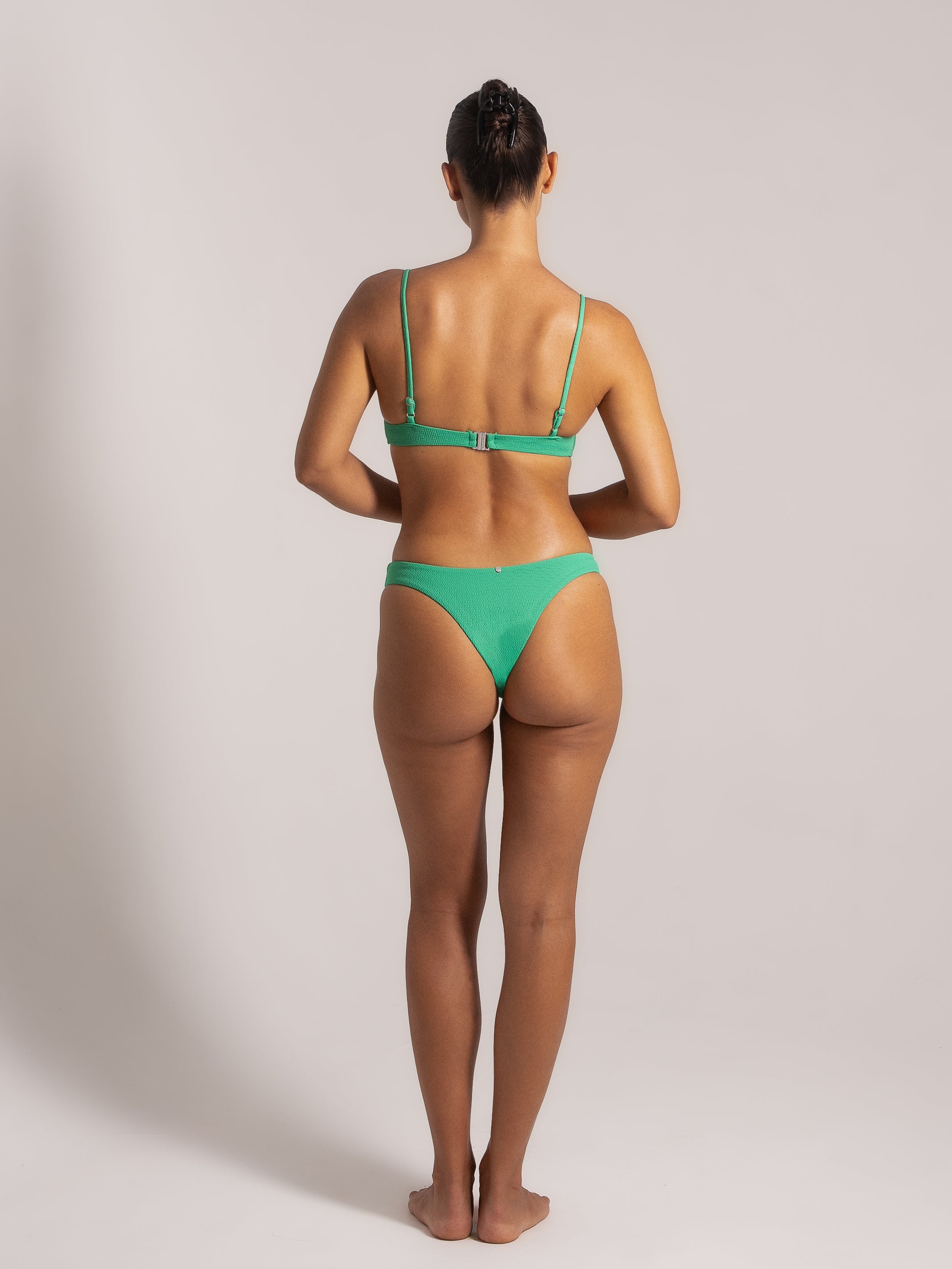 Back view of a woman in a green bikini featuring adjustable shoulder straps and a clasp closure, offering a minimal and secure fit.