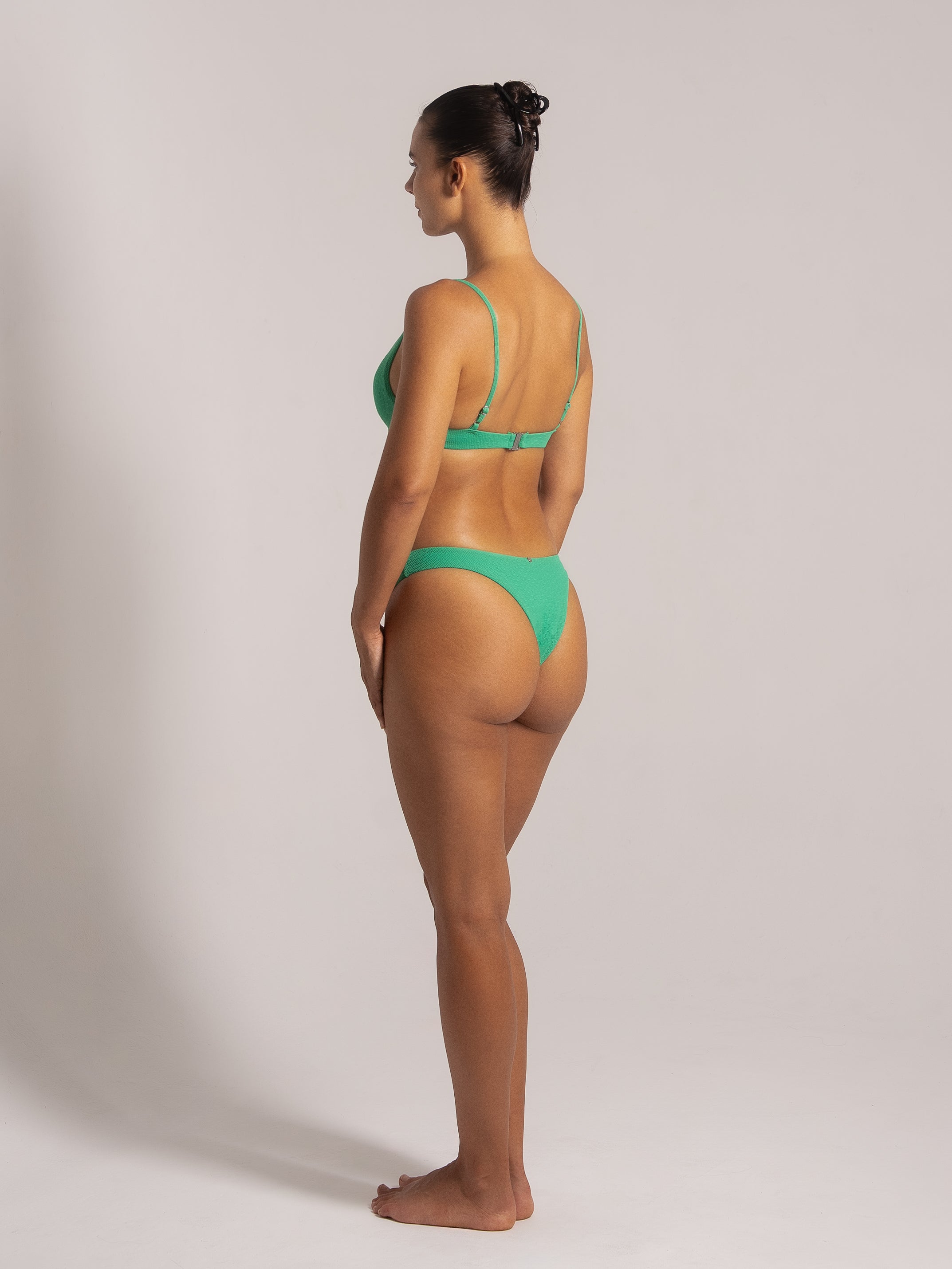 Side view of a woman modeling a green bikini with a scoop neck top and high-cut bottoms, highlighting the comfortable and stylish fit.