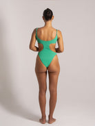 Woman wearing a green one-piece swimsuit with side cutouts, back view showcasing adjustable straps and scoop neckline.