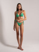 Model wearing green textured triangle bikini top with side-tie bottoms in a front pose.