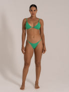 Model wearing green bikini set with V-cut top and cheeky bottoms