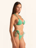Model posing in green triangle bikini top with sleek halter neckline and minimal design.