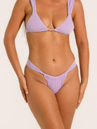 Woman wearing a high leg textured bikini bottom in lilac with V-cut waist design.