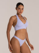 Model wearing lavender halter bikini top with embroidered texture and deep neckline