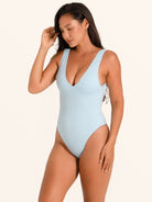 Lifestyle shot of woman in baby blue textured V neck one piece swimsuit with relaxed pose.