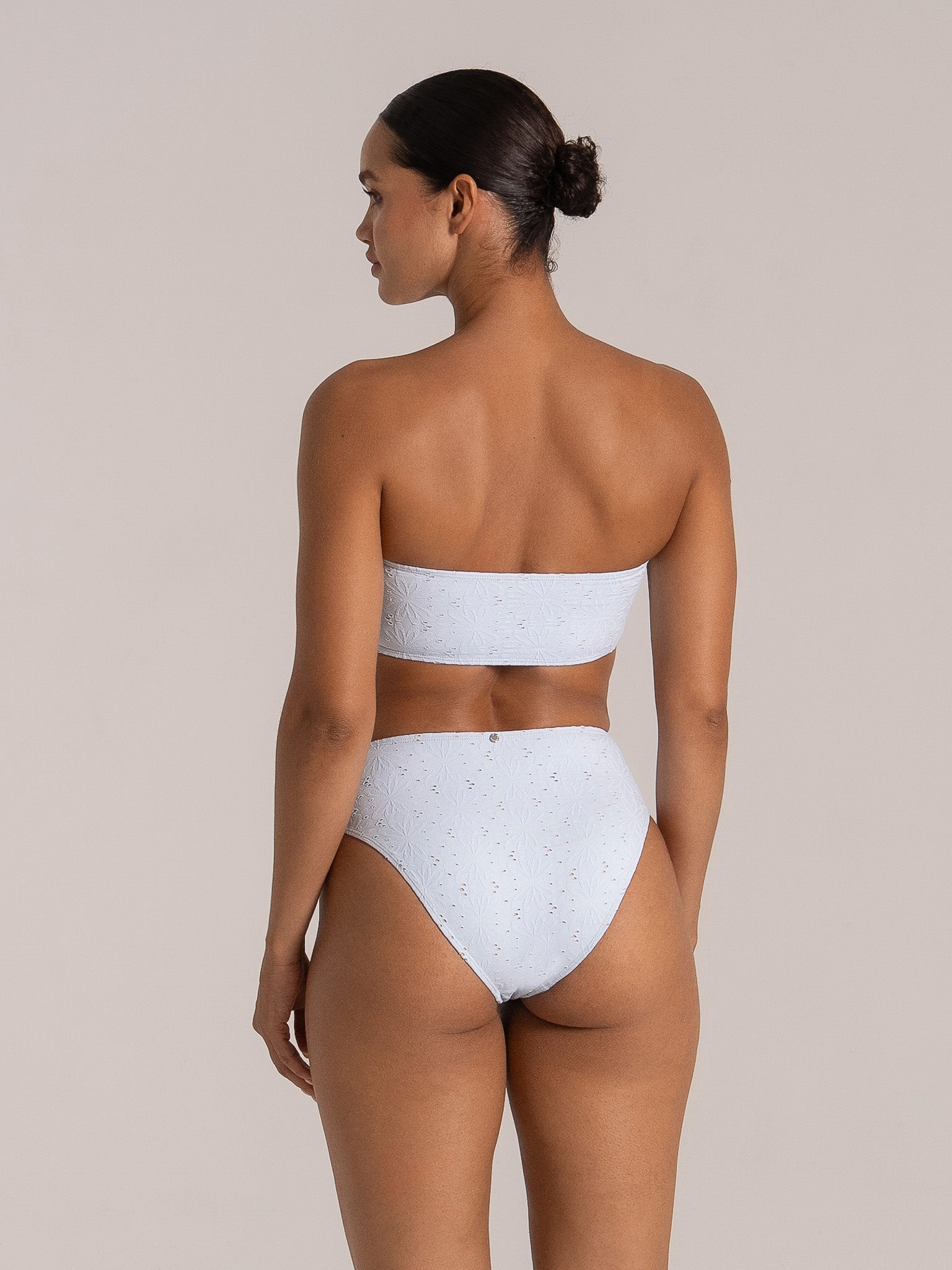 Woman wearing a light blue bandeau bikini with floral embroidery and high-waisted bottoms, back view.