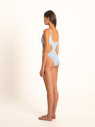 Side view of woman wearing light blue one-piece swimsuit with side cutout and scoop back