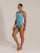 Side pose showcasing the ruched design and side-tie details of the light blue one-piece swimwear.