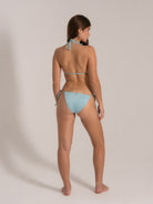 Model posing in a light blue string bikini set, side-back angle highlighting tie straps and cheeky fit