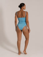 Angled back view of a light blue one-piece swimsuit featuring textured fabric and a flattering high-cut leg.