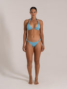 Front view of woman in a light blue textured bikini set with a halter neck triangle top and low-rise bikini bottom.
