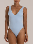 Front view of a woman wearing a light blue textured one-piece swimsuit, featuring a deep V neckline and high-cut leg openings for a sleek, minimal look.