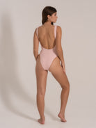 Back side view of a woman modeling a scoop-back pink one-piece swimsuit with a soft textured fabric