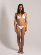 Woman wearing a light pink textured triangle bikini set with side tie bottoms, front view on neutral studio background
