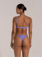 Back view of a woman in metallic light purple bikini with thin adjustable straps and minimal coverage bottom