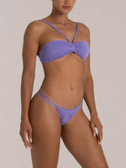Woman posing in shimmering lavender bikini with bandeau top and thin strappy bottoms, side view