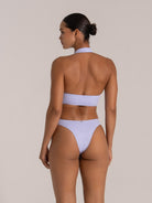 Woman wearing a light purple halter neck bikini set with floral textured fabric, back view.