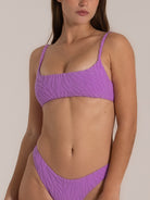 Side-angled close-up of a woman wearing a lilac bandeau bikini set with textured fabric and braided shoulder straps, styled with a matching V-cut bikini bottom.